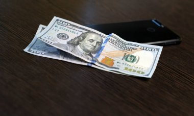 100 dolarlık banknotlar ve akıllı telefon ahşap bir masada yatıyor. Kopya alanı olan mobil bankacılık kavramı. Kapat..