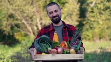 Organik çiftlikte sebze dolu tahta bir kutu tutan çiftçi. Bahçedeki gülümseyen beyaz sakallı adamın portresi..