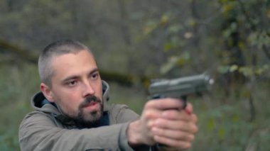 Ormandaki genç sakallı adam tabancayla nişan alır ve boğazına dayar.