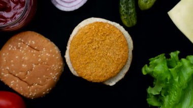 Farklı malzemelerden hamburger yapma süreci. Hareket animasyonunu durdur. Üst Manzara. Domates, soğan, marul yaprağı, sos, pirzola, salatalık, peynir