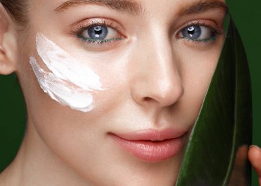 Güzel taze kız kozmetik krem yüz, doğal makyaj ve yeşil yaprakları ile. Güzellik.