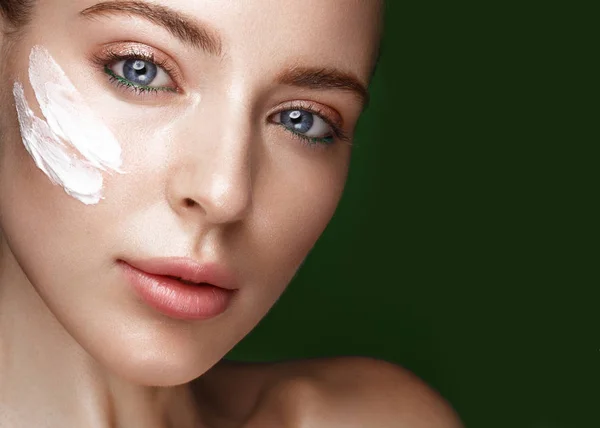 Beautiful fresh girl with cosmetic cream on the face, natural make-up and green leaves. Beauty face. — Stock Photo, Image