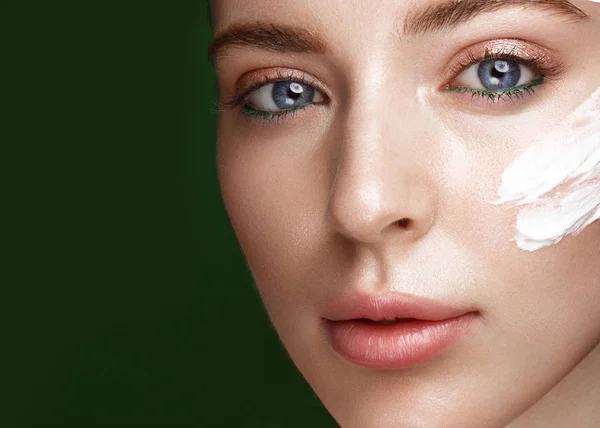 Beautiful fresh girl with cosmetic cream on the face, natural make-up and green leaves. Beauty face. — Stock Photo, Image