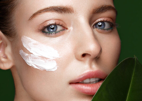 Beautiful fresh girl with cosmetic cream on the face, natural make-up and green leaves. Beauty face.