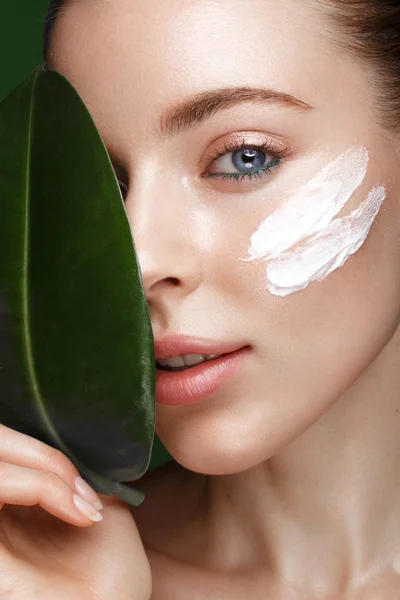 Beautiful fresh girl with cosmetic cream on the face, natural make-up and green leaves. Beauty face. — Stock Photo, Image