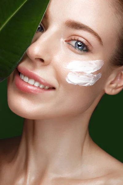 Beautiful fresh girl with cosmetic cream on the face, natural make-up and green leaves. Beauty face. — Stock Photo, Image