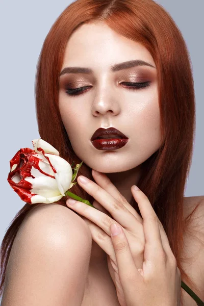Gyönyörű vörös hajú lány egy klasszikus smink és a rózsa a kezét. Szépség arc. — Stock Fotó