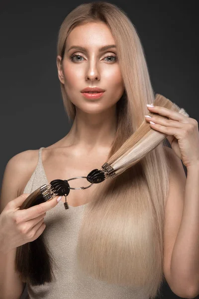 Schöne blonde Mädchen mit einem perfekt glatten Haar, klassisches Make-up mit einer Palette für Haarverlängerungen in den Händen. Schönheit Gesicht. — Stockfoto