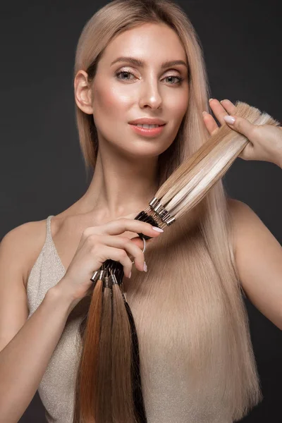 Menina loira bonita com um cabelo perfeitamente liso, clássico compõem com uma paleta para extensões de cabelo nas mãos. Cara de beleza . — Fotografia de Stock