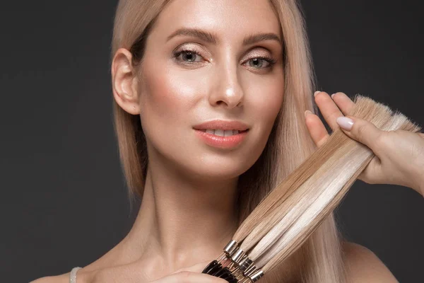 Schöne blonde Mädchen mit einem perfekt glatten Haar, klassisches Make-up mit einer Palette für Haarverlängerungen in den Händen. Schönheit Gesicht. — Stockfoto