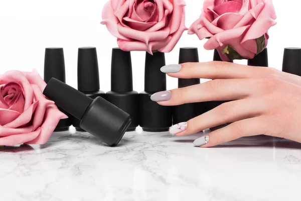 Botellas negras de esmalte de uñas sobre un fondo de flores. Diseño de manicura . — Foto de Stock