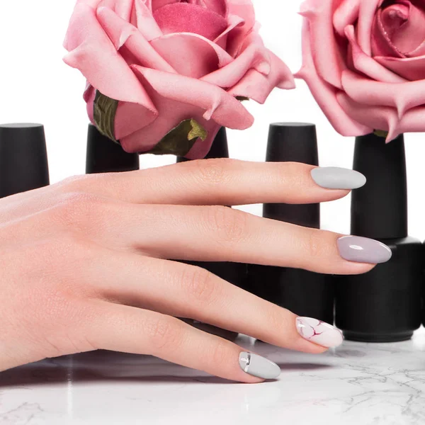 Black bottles of nail polish on a background of flowers. Manicure design.