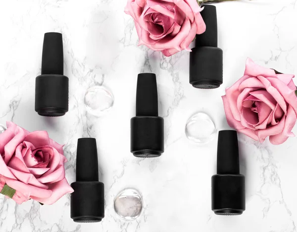 Black bottles of nail polish on a background of flowers. Manicure design.