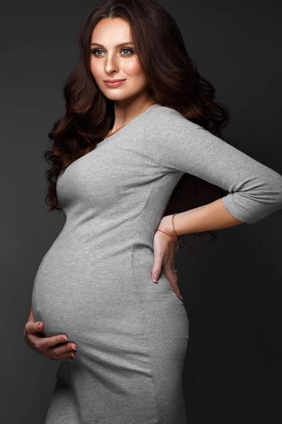Vacker gravid kvinna i en grå klänning, med en klassisk smink och lockar. Skönhet ansikte. — Stockfoto