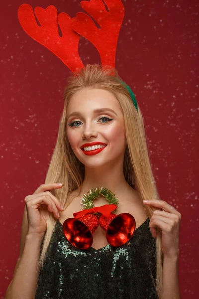 Gyönyörű szőke lány egy új év képet karácsonyi harangok körül a nyakát és a szarvas szarvak a fején. Szépség arc ünnepi smink. — Stock Fotó