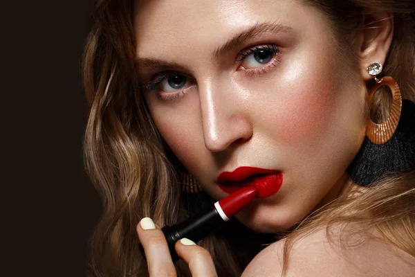 Beautiful girl with red lips and classic makeup and curls with lipstick in hand. Beauty face. — Stock Photo, Image