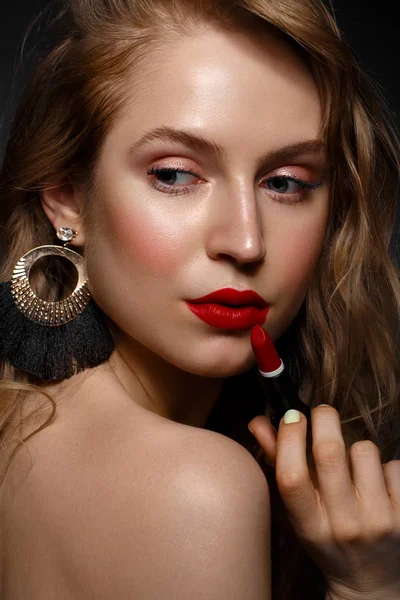Hermosa chica con labios rojos y maquillaje clásico y rizos con lápiz labial en la mano. Cara de belleza . — Foto de Stock