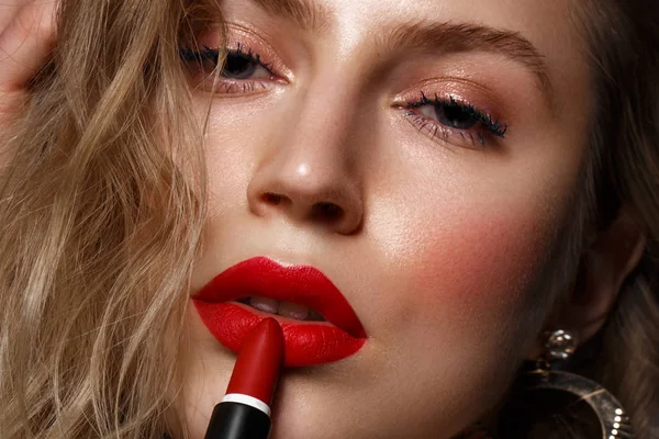 Hermosa chica con labios rojos y maquillaje clásico y rizos con lápiz labial en la mano. Cara de belleza . — Foto de Stock