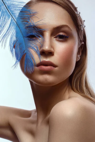 Hermosa chica bronceada con maquillaje creativo y pestañas azules, pluma en la mano. Cara de belleza . — Foto de Stock