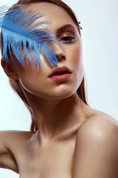 Hermosa chica bronceada con maquillaje creativo y pestañas azules, pluma en la mano. Cara de belleza . —  Fotos de Stock