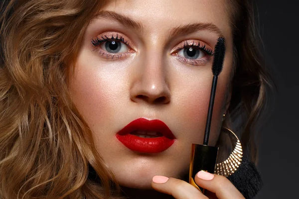 Hermosa chica con labios rojos y maquillaje clásico y rizos con rímel en la mano. Cara de belleza — Foto de Stock