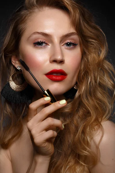 Menina bonita com lábios vermelhos e maquiagem clássica e cachos com rímel na mão. Cara de beleza — Fotografia de Stock