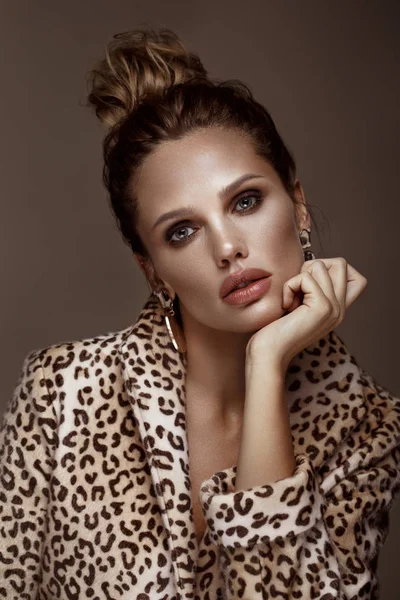 Hermosa mujer sexy en un abrigo de leopardo y pendientes, con maquillaje ahumado clásico y un peinado de moda. Cara de belleza . — Foto de Stock