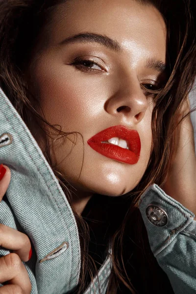 Hermosa chica sexy con maquillaje brillante, labios rojos, cabello mojado en una chaqueta de mezclilla. Cara de belleza. — Foto de Stock