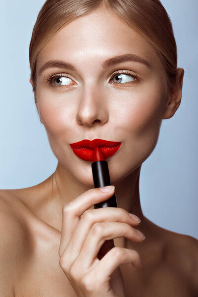 Красивая девушка с красными губами и классический макияж с помадой в руке. Красота лица
