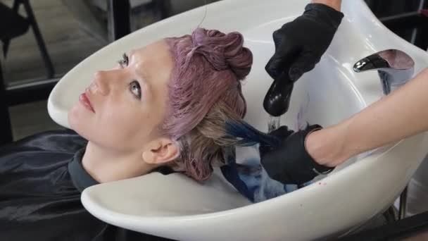 Hårfrisören tvättar bort färgen med en blond hårklient i en skönhetssalong. Studiofrisör. — Stockvideo
