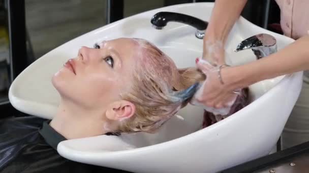 La peluquera lava la pintura con un cliente rubio en un salón de belleza. Peluquería estudio . — Vídeo de stock