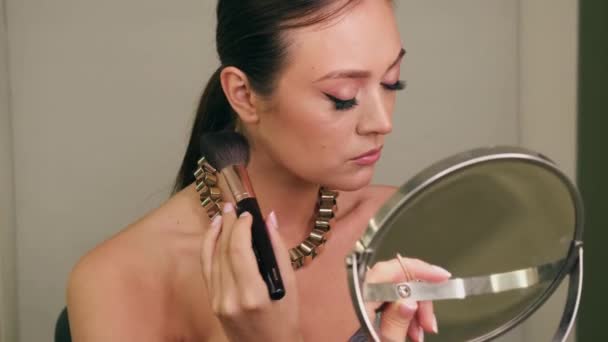 La fille applique du maquillage devant le miroir avec un pinceau à poudre. Poser devant la caméra du téléphone. — Video