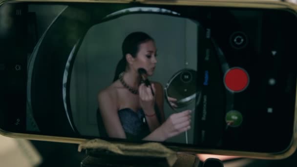 A lány sminket alkalmaz a tükör előtt egy porkefével. Pózol a telefon kamera előtt. — Stock videók