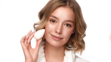 Elinde süngerle kameranın önünde poz veren beyaz önlüklü genç ve güzel bir kız. Güzel surat. Cilt bakımı.