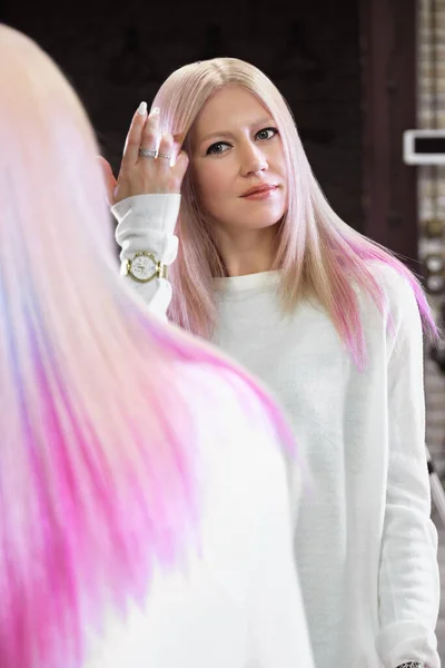 Hermosa chica rubia con el pelo de color rosa en un salón de peluquería . — Foto de Stock
