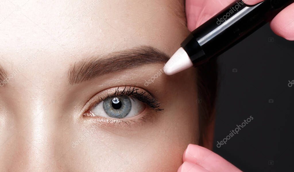Close-up of female eyes with an eyebrow highlighter. Eye makeup cosmetics.