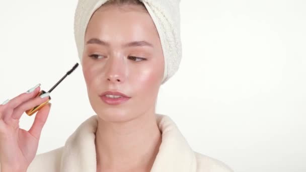 Vacker öm ung flicka i en vit handduk och badrock med ren fräsch hud poserar framför kameran. Skönhetsansikte. Hudvård. — Stockvideo