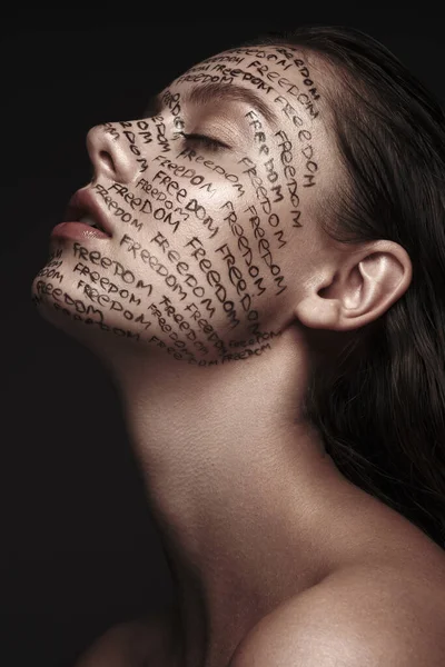 Portrait of beautiful girl with painted words on her face. Art make-up. — Stock Photo, Image