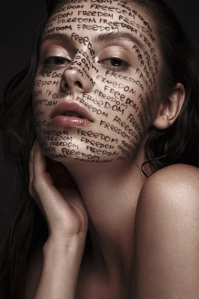Porträt eines schönen Mädchens mit gemalten Worten im Gesicht. Kunstschminke. — Stockfoto
