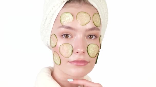 Gyönyörű, fiatal nő házi fürdőköpenyben, uborka maszkkal az arcán, pózol a kamera előtt. — Stock videók