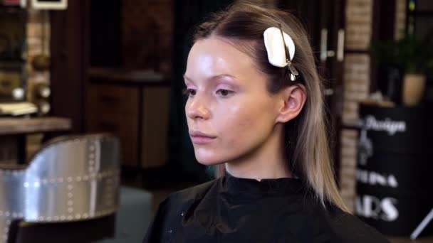 Maquillaje artista aplica cosméticos a la cara de la mujer joven en el salón de belleza. — Vídeos de Stock