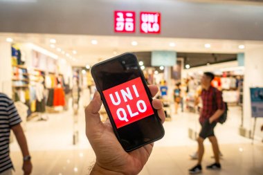 Uniqlo mağazasının önünde üzerinde Uniqlo uygulamaları olan bir iPhone X 'i tutan bir adam. Eşsiz uygulamalar online alışverişi tercih edenler için mükemmeldir