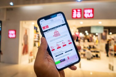 Uniqlo mağazasının önünde üzerinde Uniqlo uygulamaları olan bir iPhone X 'i tutan bir adam. Eşsiz uygulamalar online alışverişi tercih edenler için mükemmeldir