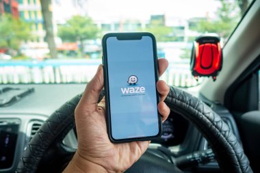 Arabanın içinde Waze navigasyon uygulaması olan iPhone X 'i tutan bir adam. Waze iyi seyrüsefer için popülerlik kazandı.