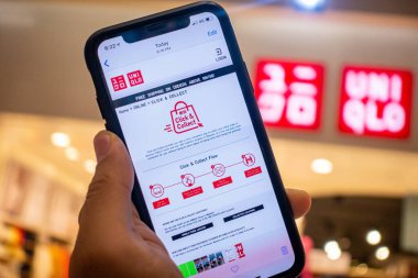 Uniqlo mağazasının önünde üzerinde Uniqlo uygulamaları olan bir iPhone X 'i tutan bir adam. Eşsiz uygulamalar online alışverişi tercih edenler için mükemmeldir