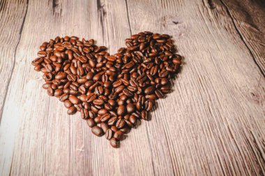 Kalp şeklinde bir avuç kahve çekirdeği, yakın plan. Masada kalp şeklinde kavrulmuş kahve çekirdekleri, seçici odaklanma. Romantik tema.