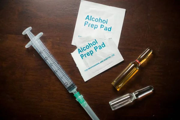 Medication ampoules for Intravenous injections on a wooden background with empty syringe and alcohol swab, medical concept