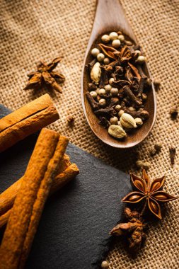 Bir paçavranın tepesindeki tahta kaşıkta çeşitli baharatlar.