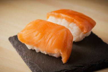 Somon nigiri sushi, siyah bir tabakta servis edilir, seçici bir odak noktası vardır.