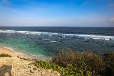 Pandawa Sahili 'nde geniş bir açı, Bali' de kumlu sahilde şemsiyeler, okyanusta güçlü dalgalar ve mavi bir gökyüzü.